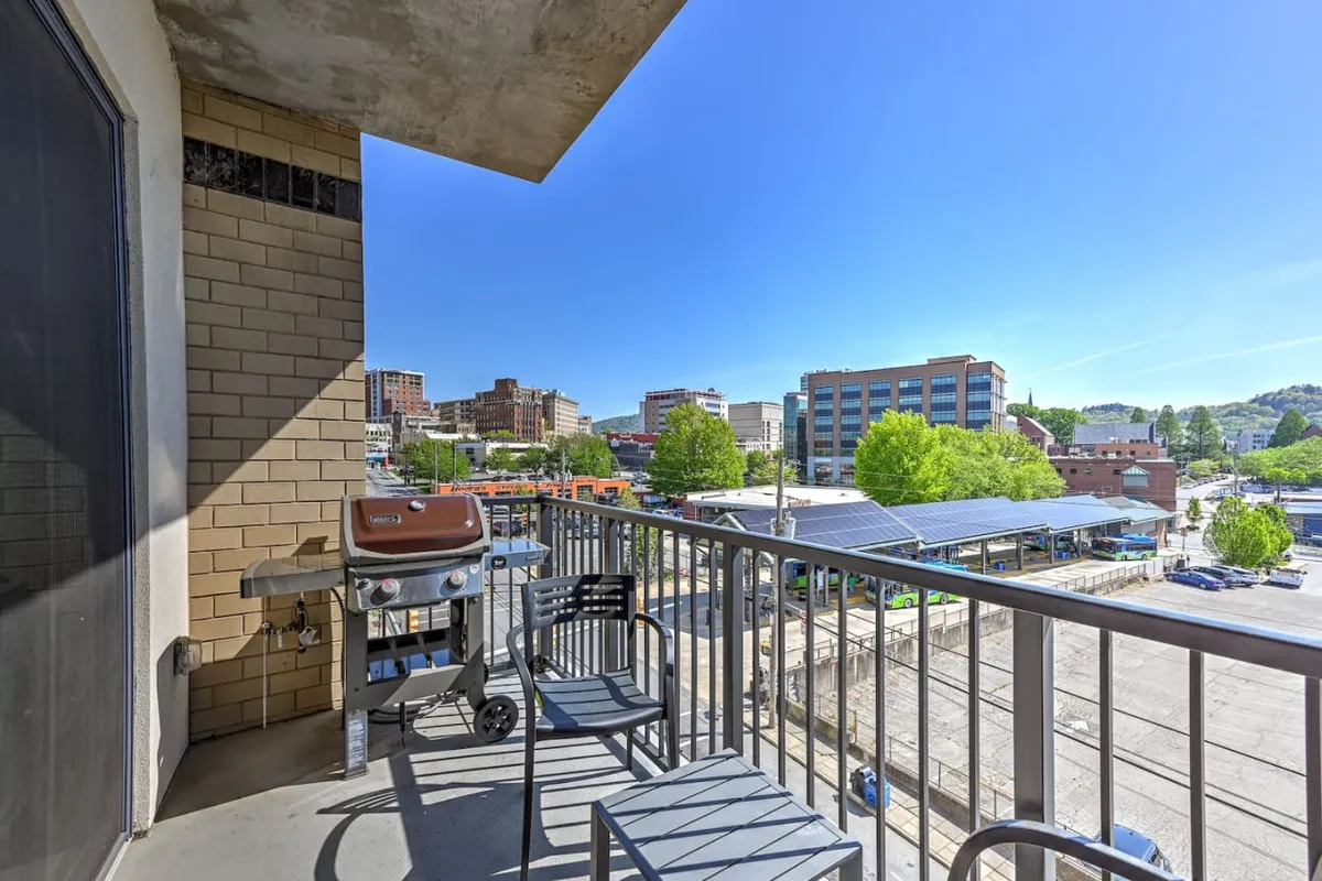 A private balcony featuring outdoor seating, a barbecue grill, and a railing overlooking the vibrant city below. The view suggests opportunities for morning coffee, evening drinks, or simply soaking in Asheville’s energy from above.
