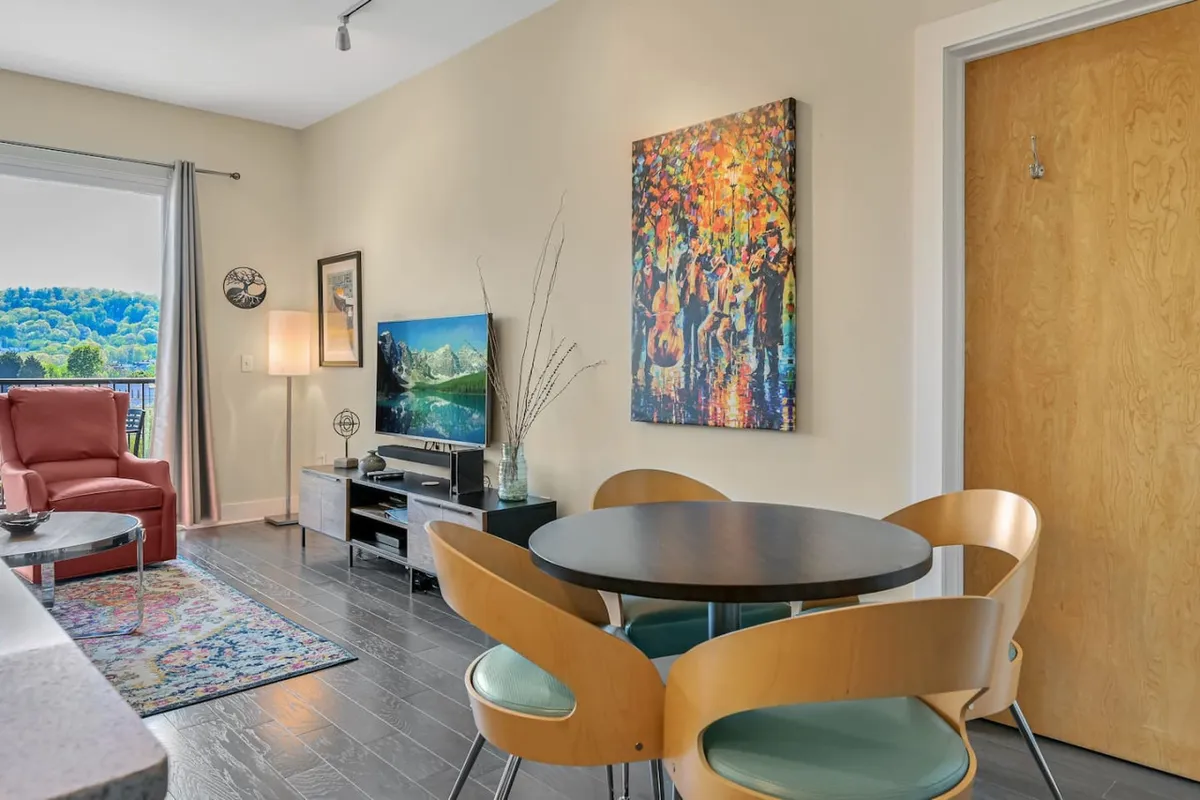 A bright, welcoming living/dining space with colorful artwork, a dining table, sofa, and television. The area is arranged for group gatherings, casual meals, or relaxing evenings after a day of exploration.