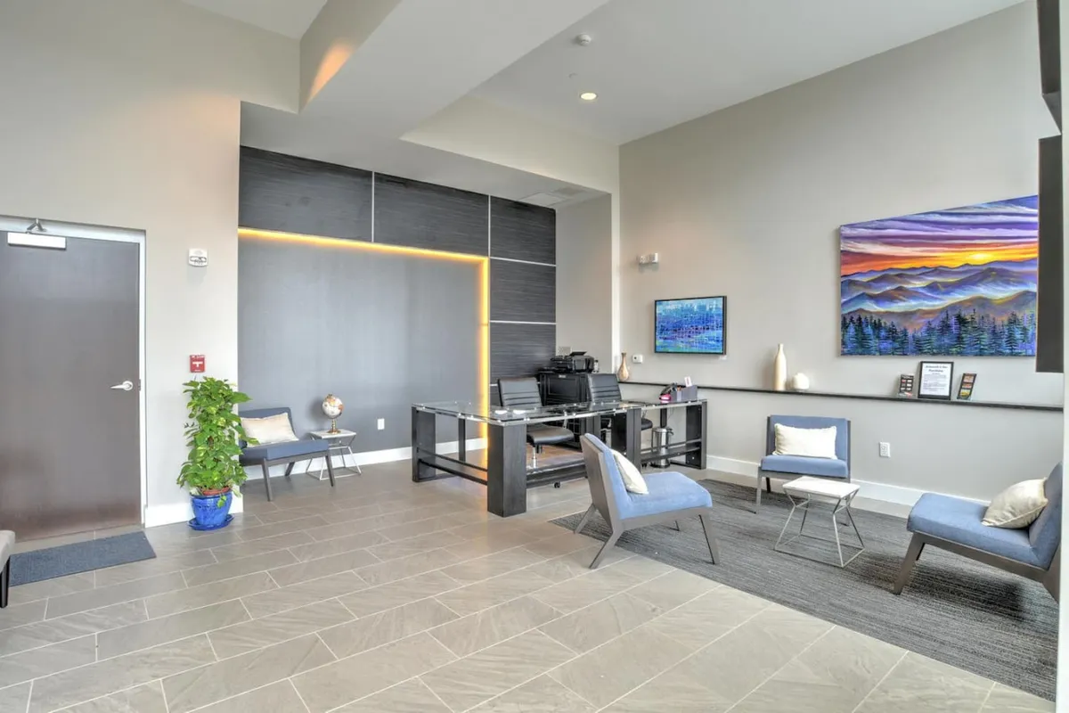 An inviting interior lobby space featuring a modern desk, comfortable seating, elegant artwork, and a touch of greenery. The setting suggests a secure, stylish entry point to the residence.