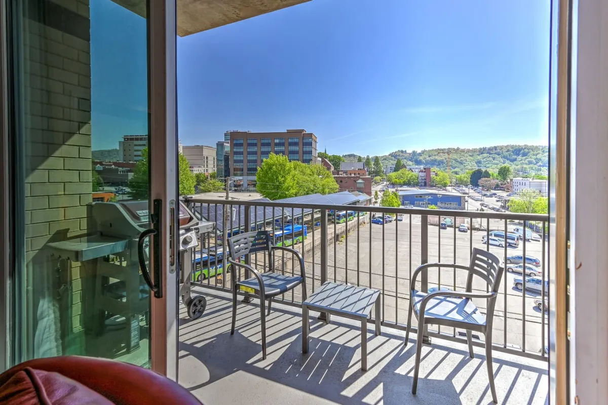 A private balcony with comfortable chairs overlooks the city landscape below, inviting residents to relax, socialize, or simply enjoy the sights and sounds of urban life. The railing frames a sweeping view of downtown activity.